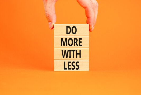 Do more with less symbol. Concept word Do more with less on beautiful wooden block. Beautiful orange table orange background. Businessman hand. Business do more with less concept. Copy space.