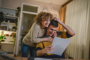 Young man and his mother woman hold paper read good news in letter sit at desk at home beautiful female received correspondence bank statement or notification invitation scholarship pleasant message - obrazy, fototapety, plakaty