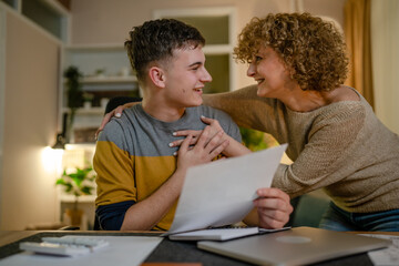 Young man and his mother woman hold paper read good news in letter sit at desk at home beautiful...