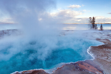 Black Pool hot spring in the West Thumb Geyser area of Yellowstone Lake in Yellowstone National Park with snow in winter at sunset.