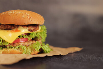 Double cheeseburger on a gray background. Juicy tasty burger on craft paper, side view. Fast food. Copy space