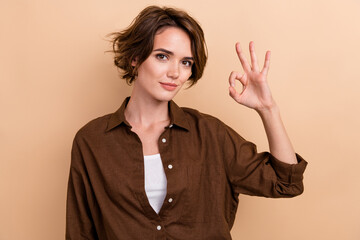 Photo of cool confident lady wear brown shirt smiling showing okey gesture isolated beige color background