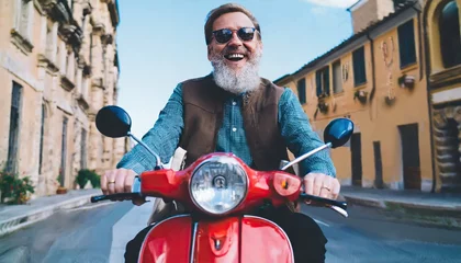Deurstickers Excited senior man riding red scooter in Italy, cheerful retired bearded hipster enjoying holiday, motorcycle road trip, trendy vacation lifestyle © Marko