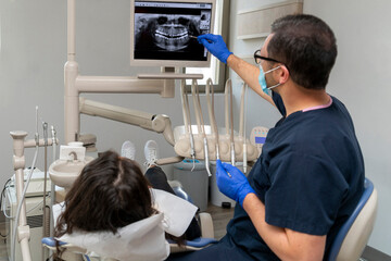 dentist gives information to her patient by showing dental x-ray showing and looking computer screen