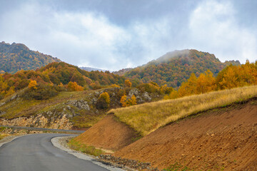 Winding road to the mountains. Sunny autumn in the mountains covered with bright colorful trees.