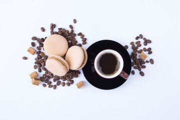 Black coffee in the brown cup, macaron and roasted coffee beans on the white background. Top view.