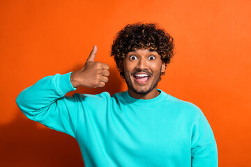 Photo of handsome astonished american guy demonstrate thumb up approve isolated on orange color background