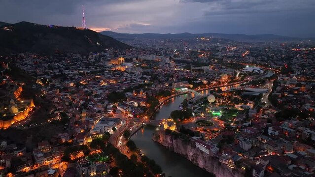 Tbilisi, Georgia. Scenic aerial view at twilight Of Famous Landmarks In Night Illuminations. Cityscape. Overview of the Kura (Mtkvari) River in Old Town, Tbilisi city central park and Bridge of Peace