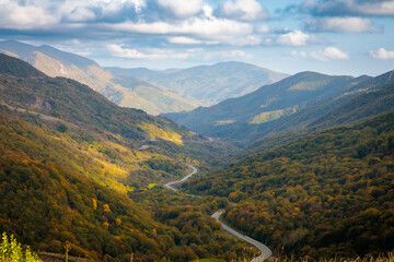 Obraz premium Winding road to the mountains. Sunny autumn in the mountains covered with bright colorful trees.