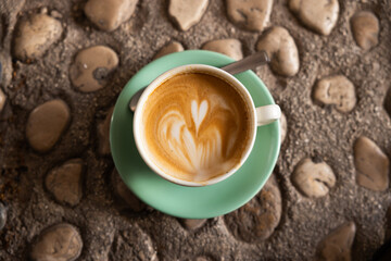 cup of coffee with heart shape foam latte sits on stone walkway in Europe on a summer morning