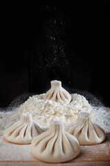 Cooking dumplings or cooking khinkali. Traditional Georgian dish. Dumplings are made by hand. Close-up. Vertical photo. Black background. Copy space.