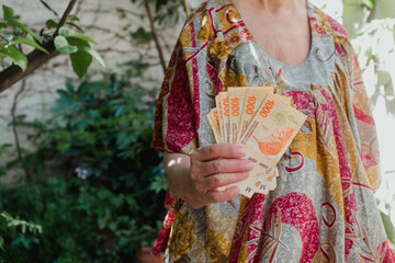 Elderly woman holding argentine pesos. Financial concept related to inflation and economic crisis.