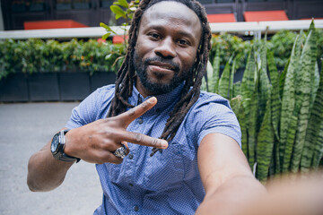 portrait of black man with dreadlocks looking at camera making v sign with fingers and laughing