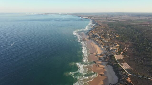 Aerial view of Praia do Malhao beach at sunrise with fog and haze in Portugal Sines. Bird's eye view of waves with turquoise water.