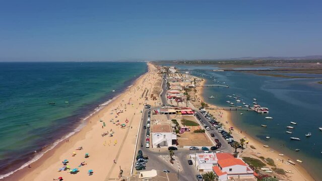 Aerial view of the ocean coast and beach. Boats on the water and tourists relaxing on the beach as seen from a drone. Praia de Faro Algarve Portugal. Movement frontally forward