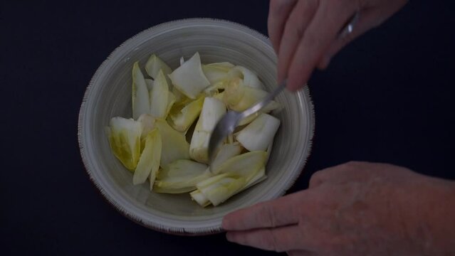 Stirring an endive salad with a fork.