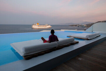 Man relaxes on the sunbed during sunset time at Mykonos, Greece