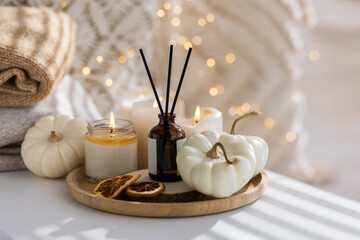 Obraz na płótnie Canvas Home comfort, coziness, aromatherapy. Cozy interior with knitting, burning candles and aroma perfume diffuser in the living room. Pumpkin spicy sweet pie fall fragrance, autumn scent, relaxation