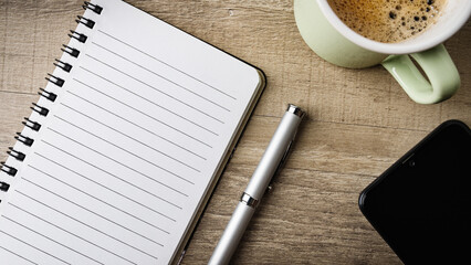 Notepad, a mobile phone, a pen and a cup of coffee on a rustic desktop