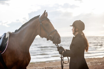 Equestrian sports. Horsewoman and her horse on the beach, portrait on the background of the sea,...