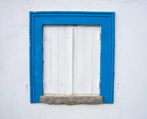 Janela tradicional algarvia numa típica casa em Portimão. Janela de madeira pintada de branco com a guarnição em azul e parede também branca. 