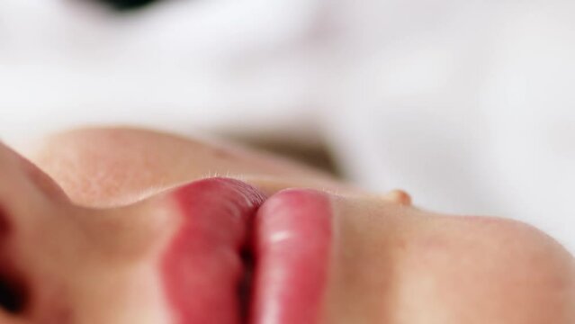 Permanent makeup procedure applying rose red pigment using tattoo machine in beautician salon. Microblading tattoo lips, close up	