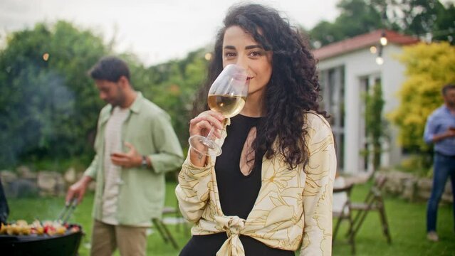 Portrait of beautiful woman holding glass with alcohol and drinking, while posing in front of camera. Young woman having fun at home party outdoors. Concept of friends, holidays and leisure time.