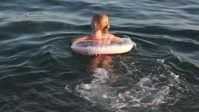 Little girl swims with an inflatable ring in the sea.