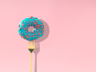 Yummy blue glazed donut pricked on a fork on pastel pink background. Creative art. Contemporary...