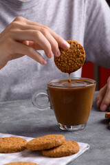 Woman's hand dipping a cookie into a transparent cup with coffee with milk in the kitchen, have italian breakfast, food lifestyle, close up