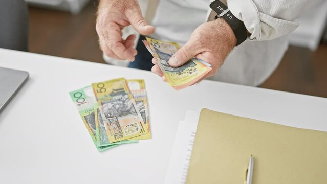 Handsome middle-aged caucasian business man counting stacks of australian dollars in office, taking investment success in stride