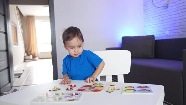 Little kid in blue t-shirt runs up to a desk. Lovely toddler sits down to play a game of puzzles.