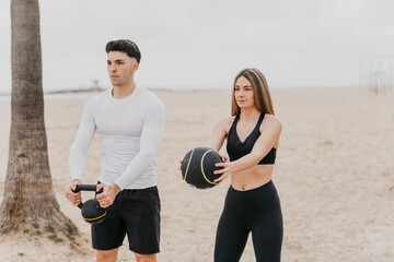 Young athletic couple exercising at the beach with a kettlebell and a medicine ball