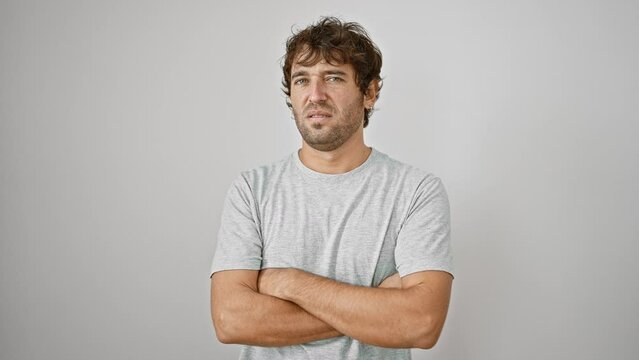 Young doubt-filled man, skeptic, nervously crosses arms. disapproving face, negative expression against isolated white background - portrait of a casual t-shirt guy looking displeased.