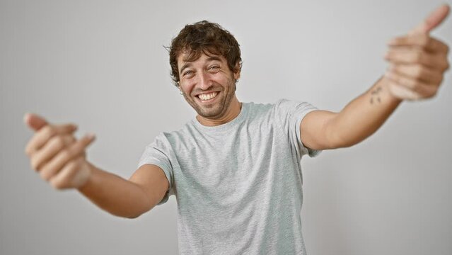 Joyful young man in casual t-shirt, arms wide open for a friendly hug, smiling at camera. embracing happiness against an isolated white background. come on, feel the love!