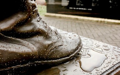 Closeup shot of rain droplets on the boot of a bronze memorial statue