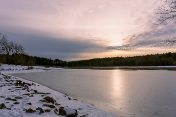 Scenic view of bright sunset cloudscape over frozen lake in Massachusetts in winter