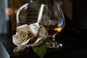 Closeup of sheet music boutonniere next to a glass of whiskey on the table - obrazy, fototapety, plakaty