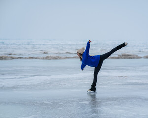 Caucasian woman in a blue sweater is skating on a frozen lake. Figure skater performs a swallow. 