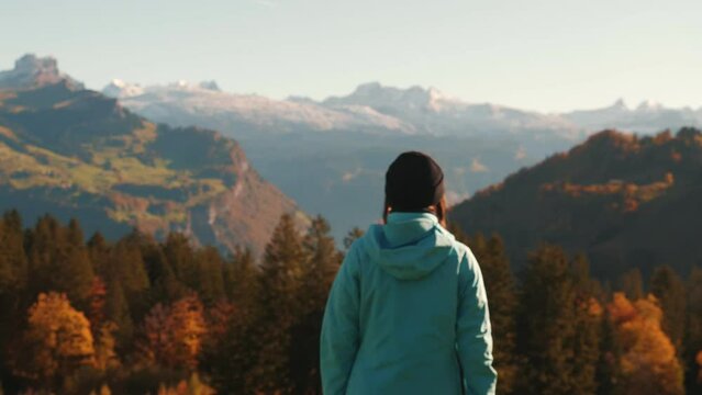 Female hiker standing on edge of hill and looking at snowy swiss Alps mountains
