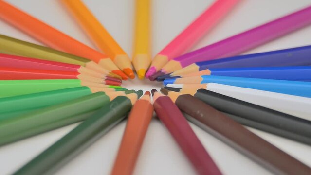 multi-colored pencils lie on a white background. Bright colored pencils rotate around themselves.