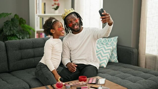 African american father and daughter wearing king crown and baggy eyes pad make selfie by smartphone at home