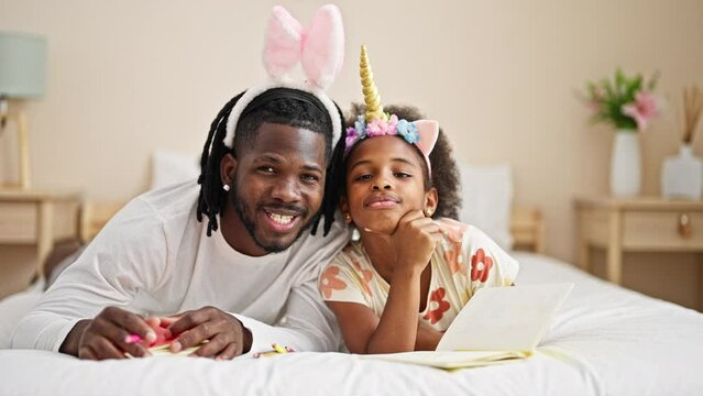 African american father and daughter wearing funny diadem lying on bed smiling at bedroom