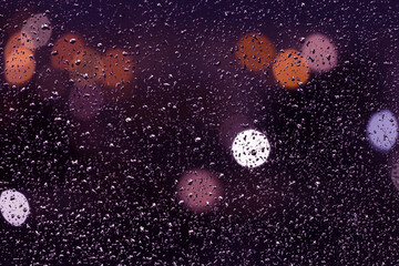 Rain drops on window glass at night with blurred bokeh light close up macro. Unfocused abstract lights background texture