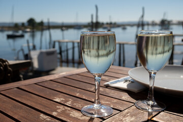 Drinking of white wine at farm cafe in oyster-farming village, with view on boats and water of Arcachon bay, Cap Ferret peninsula, Bordeaux, France - obrazy, fototapety, plakaty