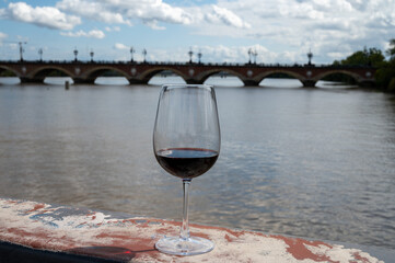 Tasting of Bordeaux blended red wine with wine city Bordeaux on background, left bank of Gironde Estuary, France. Glass of red French wine.