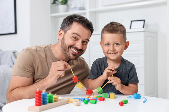 Motor skills development. Father and his son playing with wooden pieces and string for threading activity at table indoors