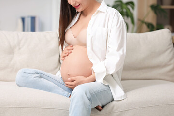 Pregnant woman sitting on sofa at home, closeup