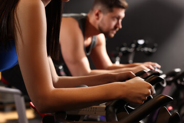 Fototapeta na wymiar Woman and man training on exercise bikes in fitness club, closeup