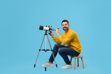 Happy astronomer with telescope on light blue background